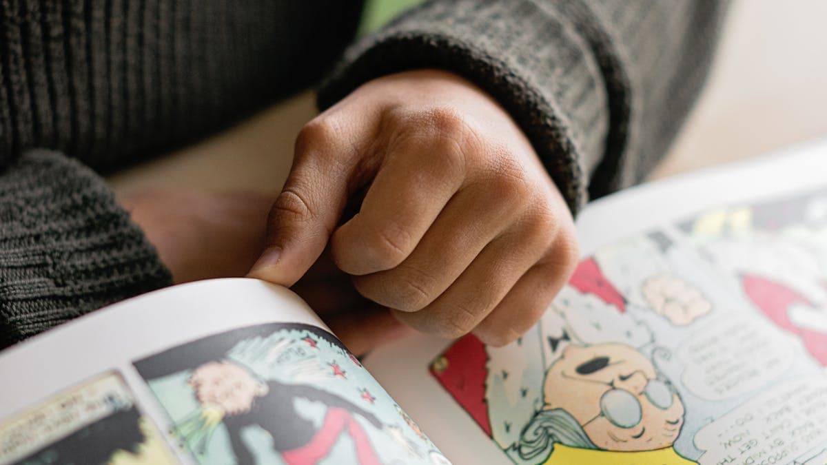 Child's hands turning the pages of a colourful comic book