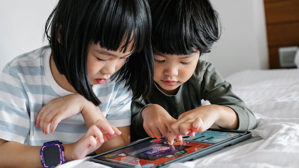 Two Asian children playing a game on a tablet together