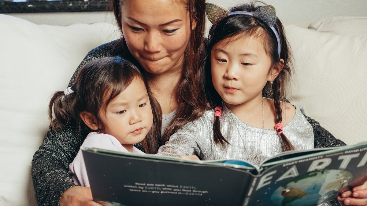 Asian mother reading an educational book with her two young daughters at home